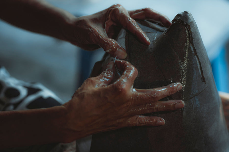 Artisan hands shaping a large wet-clay vessel in a workshop.
