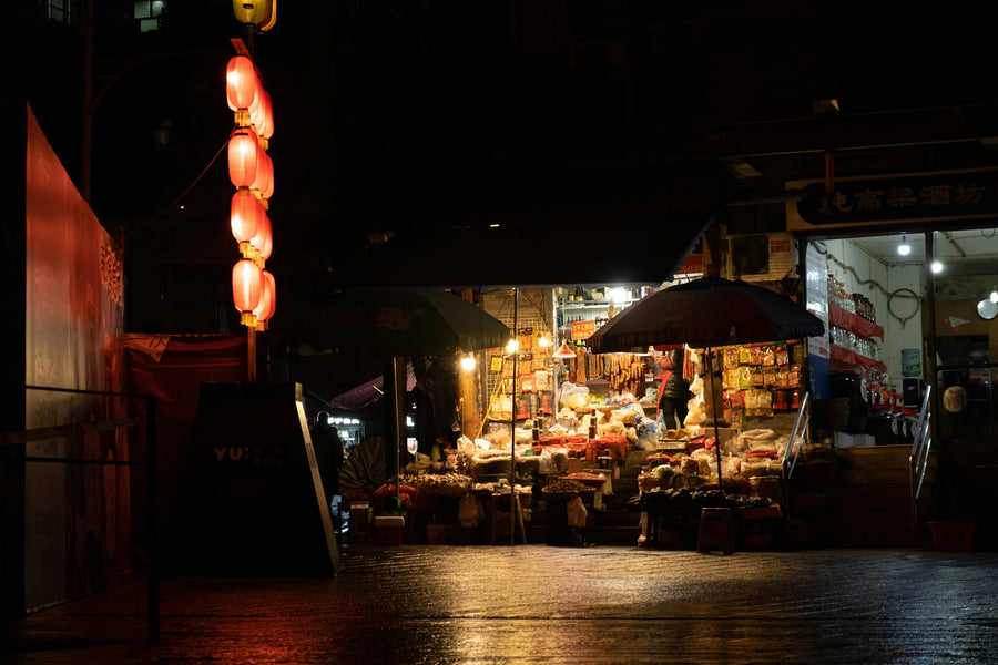 Lanterns and an illuminated food stall reflected on wet pavement at Huashi night market in Chongqing.