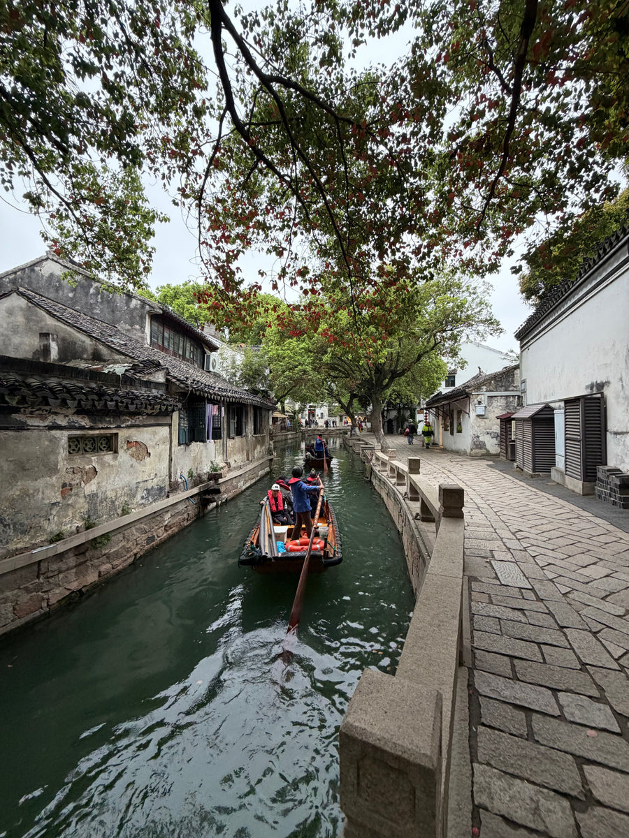 Traditional wooden boat travelling along a narrow historic canal in Suzhou.