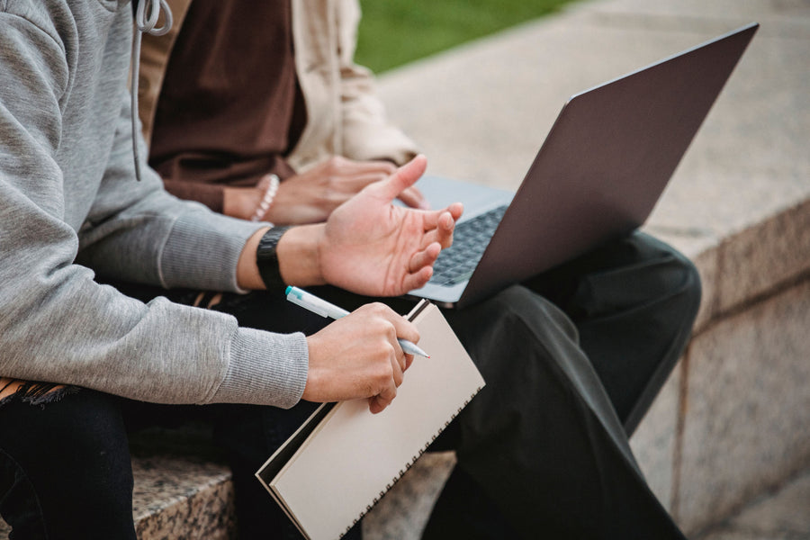 Two university students collaborating with a laptop and notebook outdoors.