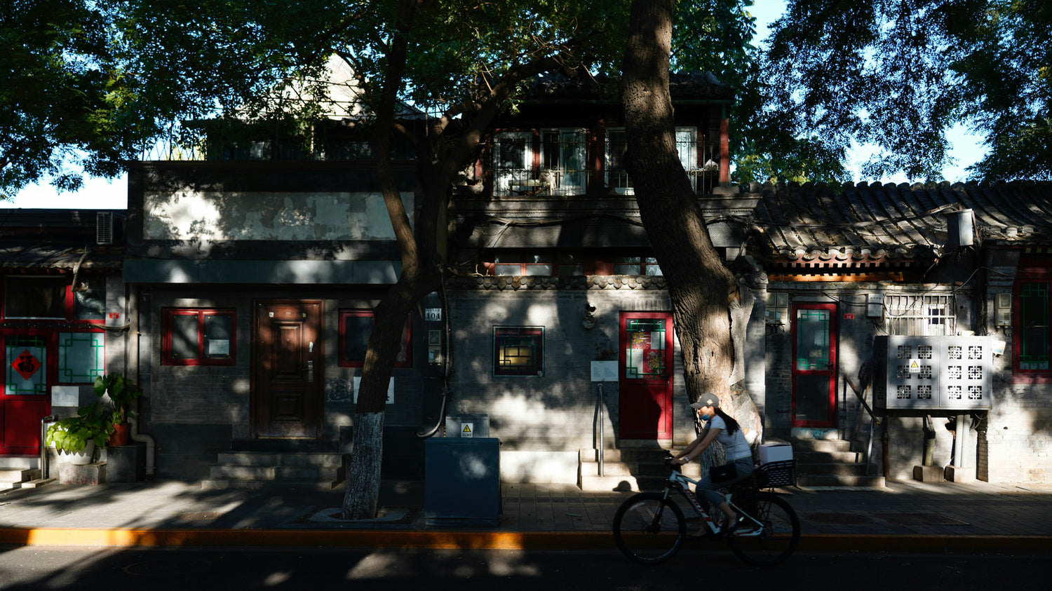 A cyclist passes shaded courtyard homes in a Beijing hutong.