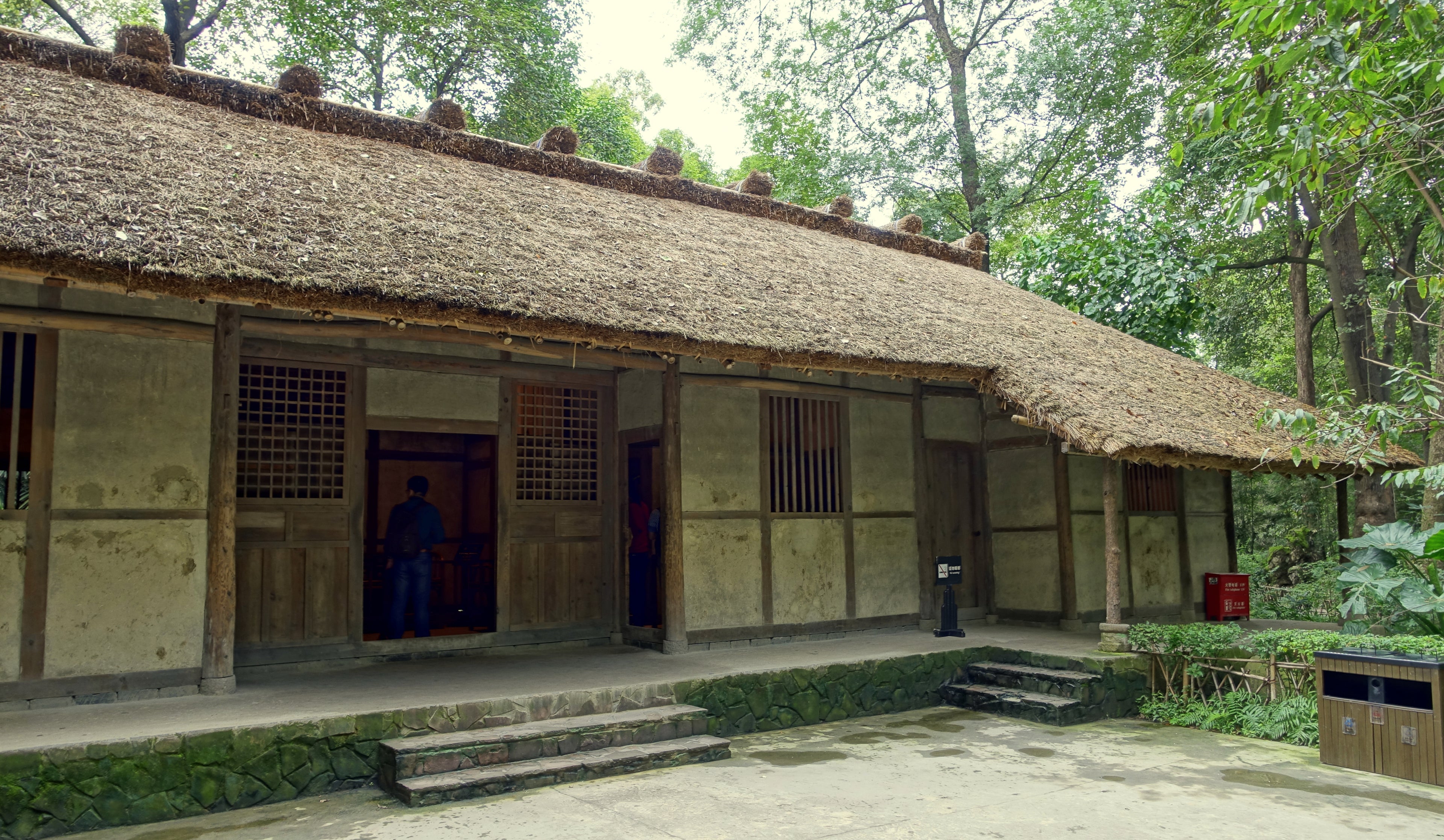 Du Fu's thatched cottage in Chengdu, with two visitors seen from behind at the doorway.