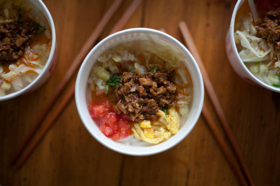 Three bowls of a traditional Chinese noodle breakfast with vegetables, egg and meat toppings.
