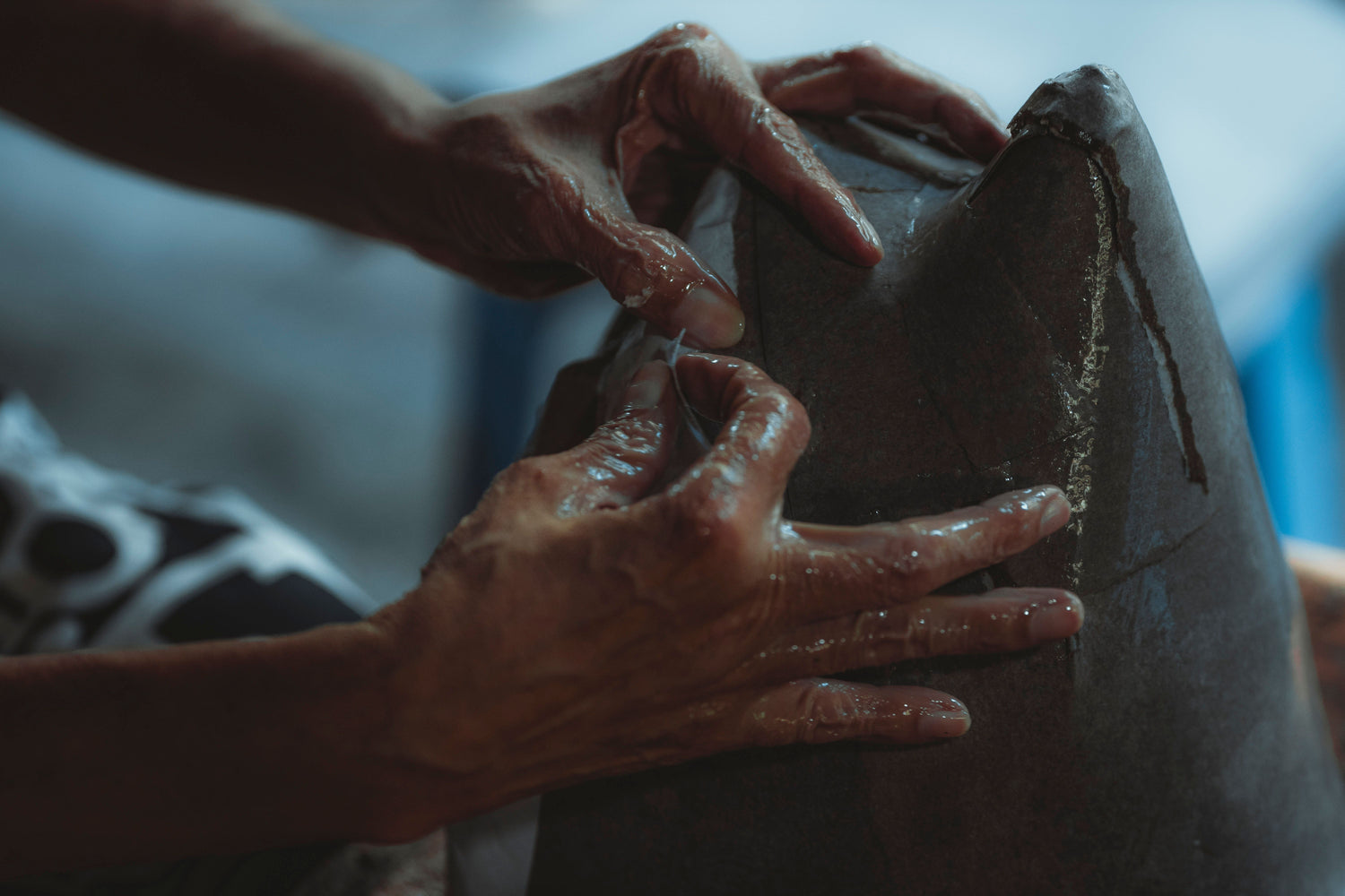 Artisan hands shaping a large wet-clay vessel in a workshop.