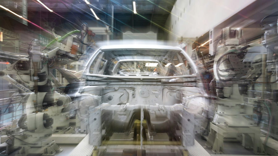 Robotic arms working around an unpainted car body on an automated assembly line.