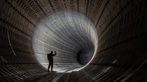 Silhouetted visitor standing inside a vast curved industrial tunnel.