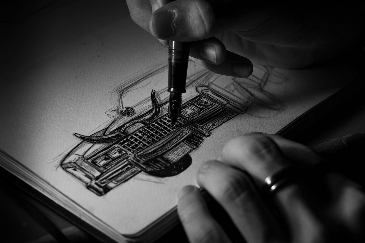 Hands drawing a detailed automobile design sketch in a notebook.