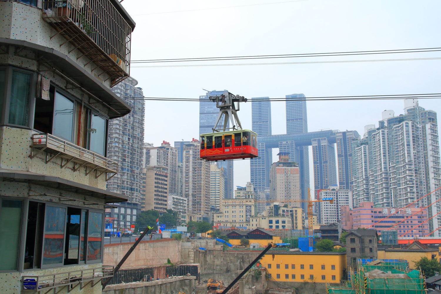 A red Yangtze River cable car crossing between dense high-rise buildings in Chongqing.