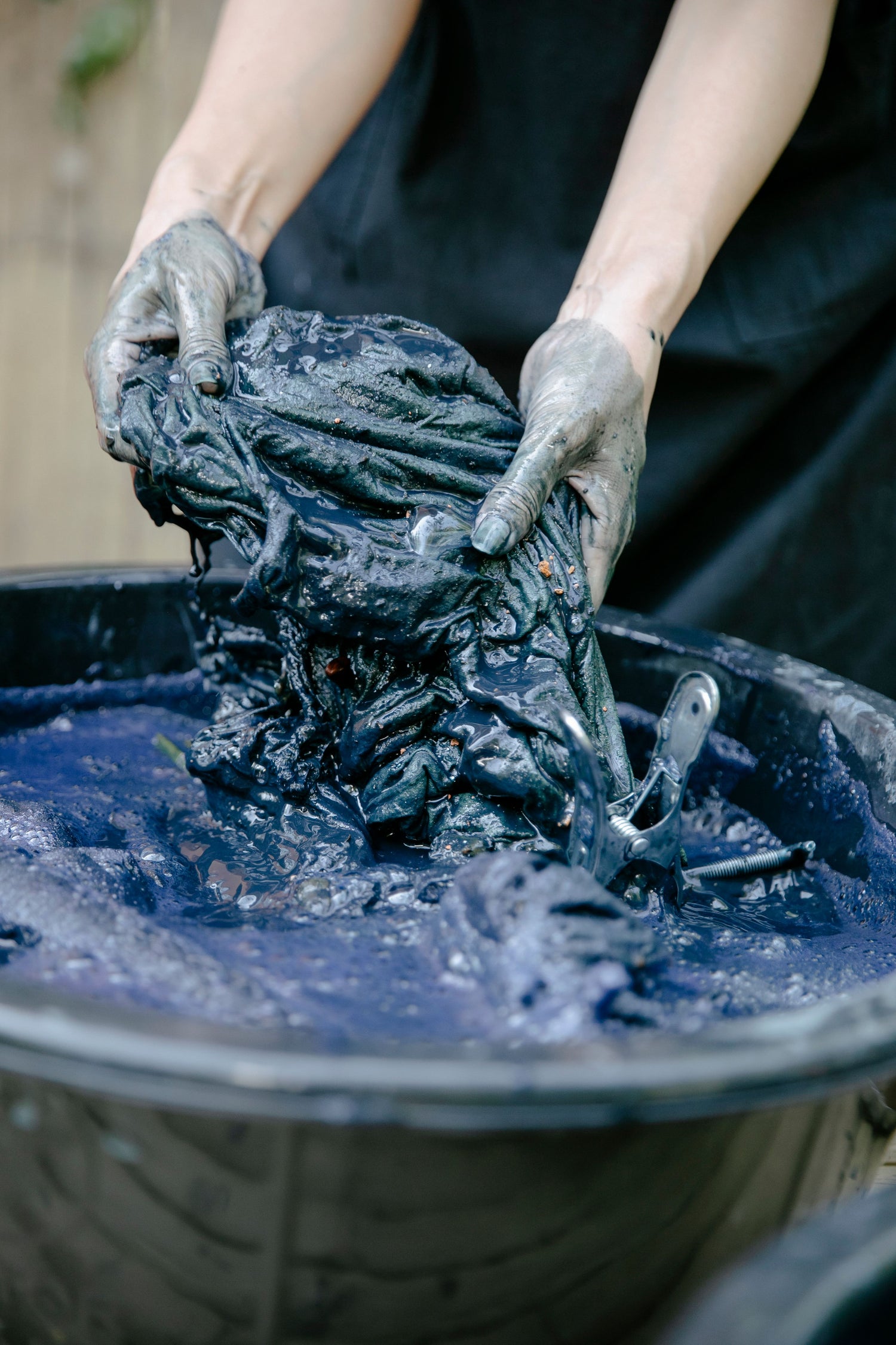 Indigo-stained hands lifting wet dark-blue fabric from a dye vat.