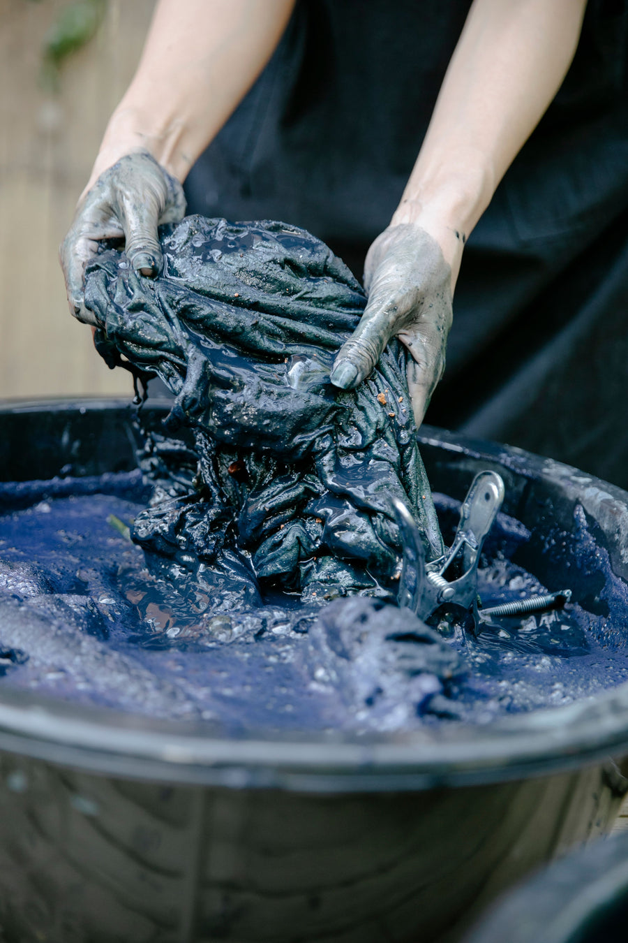 Indigo-stained hands lifting wet dark-blue fabric from a dye vat.