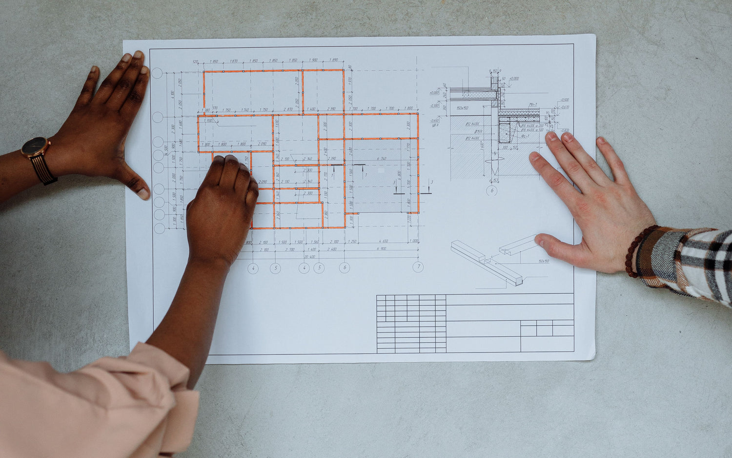 Two collaborators’ hands reviewing an architectural floor plan.