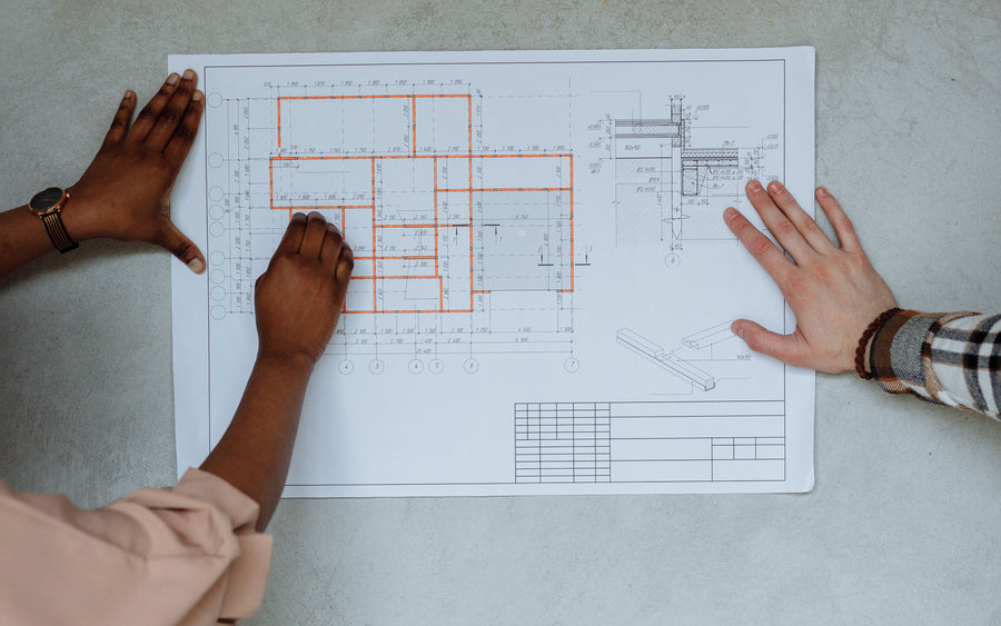 Two collaborators’ hands reviewing an architectural floor plan.