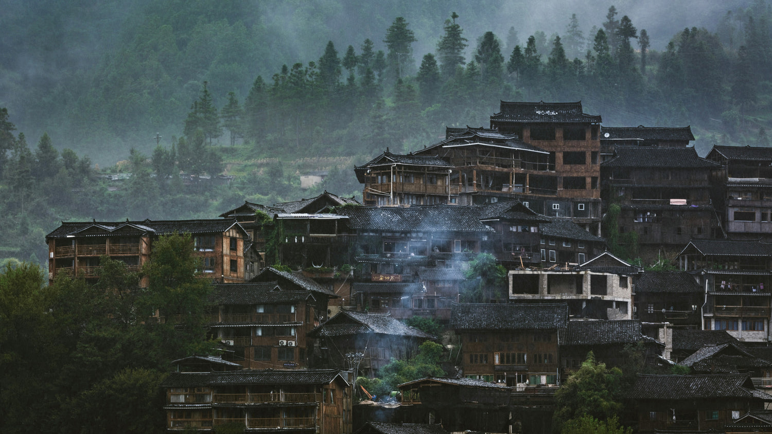 Wooden hillside houses in morning mist at Xijiang Miao Village in Guizhou.