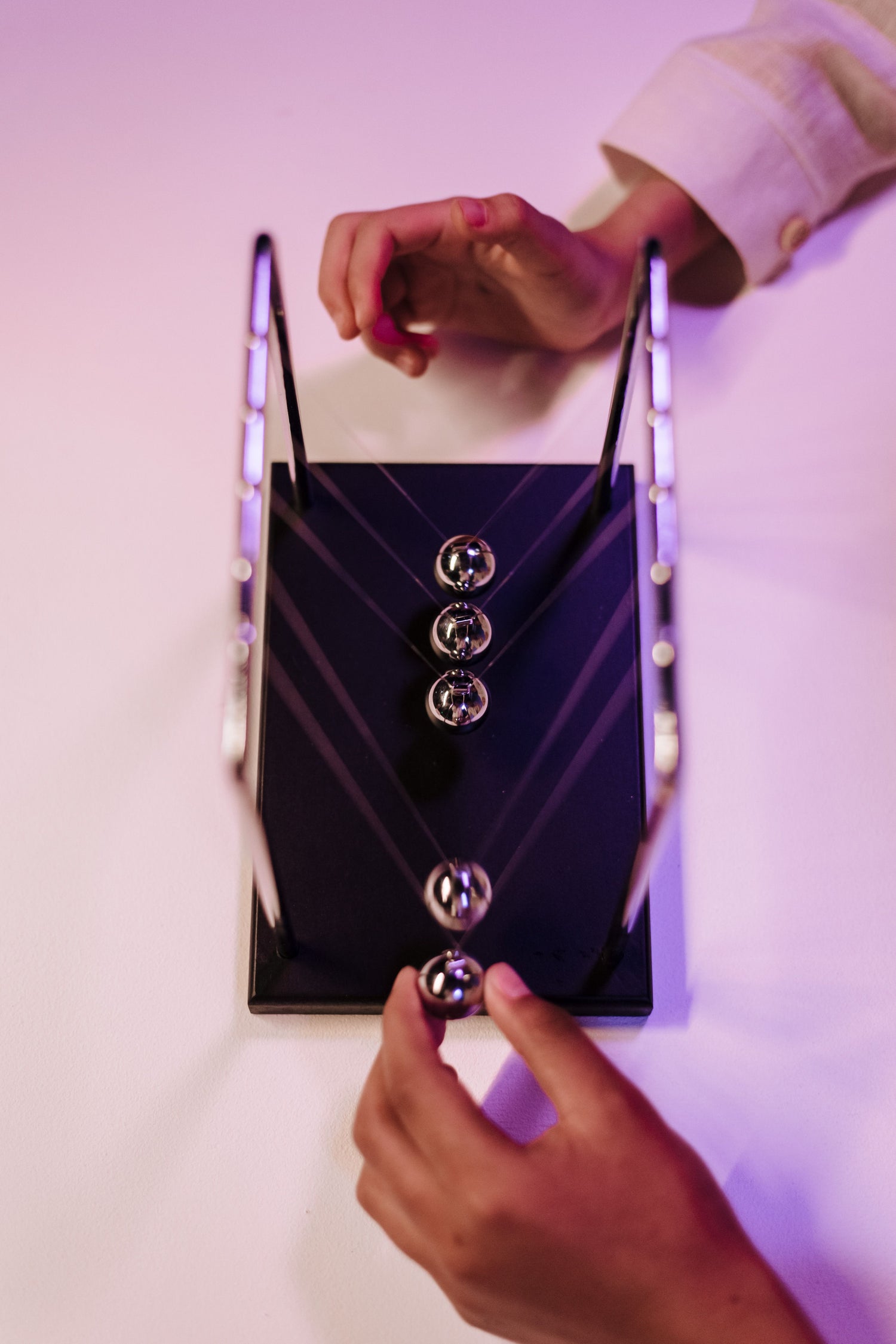 A hand setting a Newton’s cradle in motion during a physics demonstration.