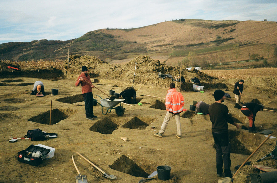 An archaeology team excavating trenches in a field with hand tools and survey equipment.