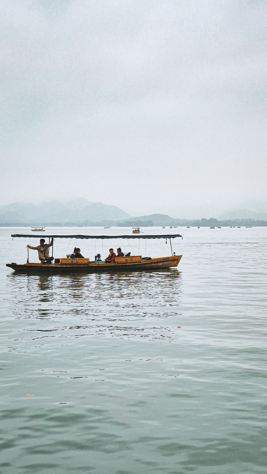 A traditional passenger boat crossing misty West Lake in Hangzhou.