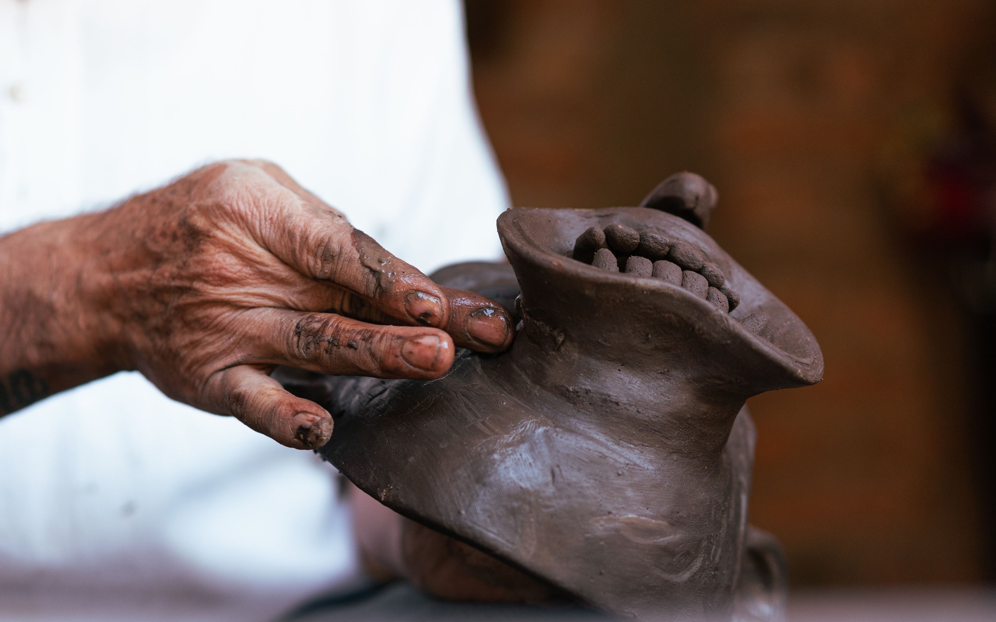 An artisan’s clay-covered hand shaping the mouth of a handmade clay mask.