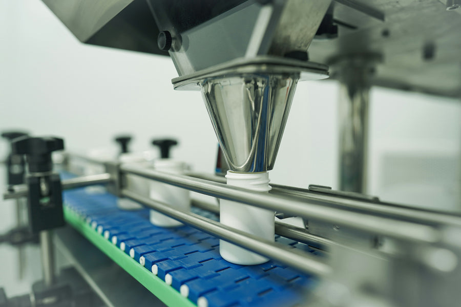 White bottles moving beneath a stainless-steel filling head on an automated production line.