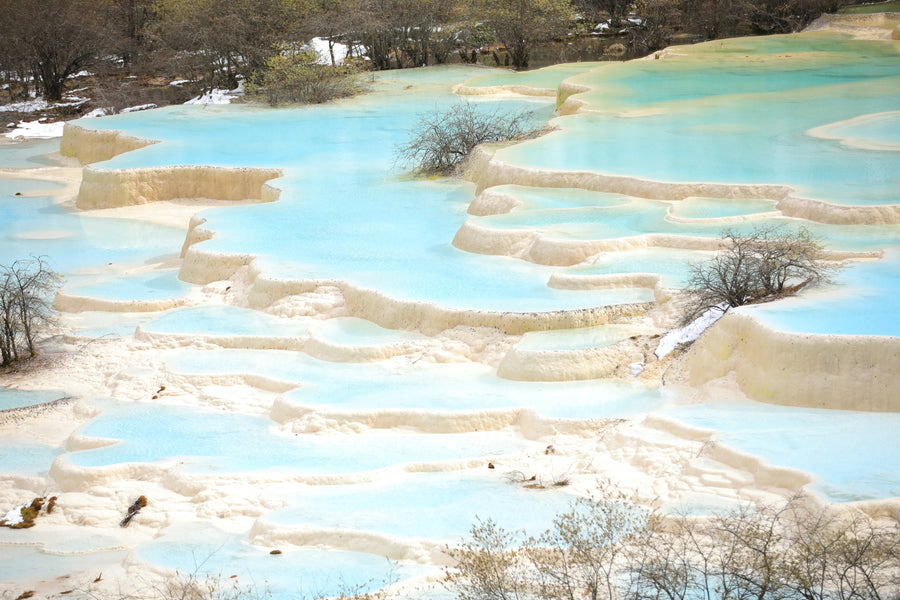 Turquoise water flowing through broad white travertine terraces.