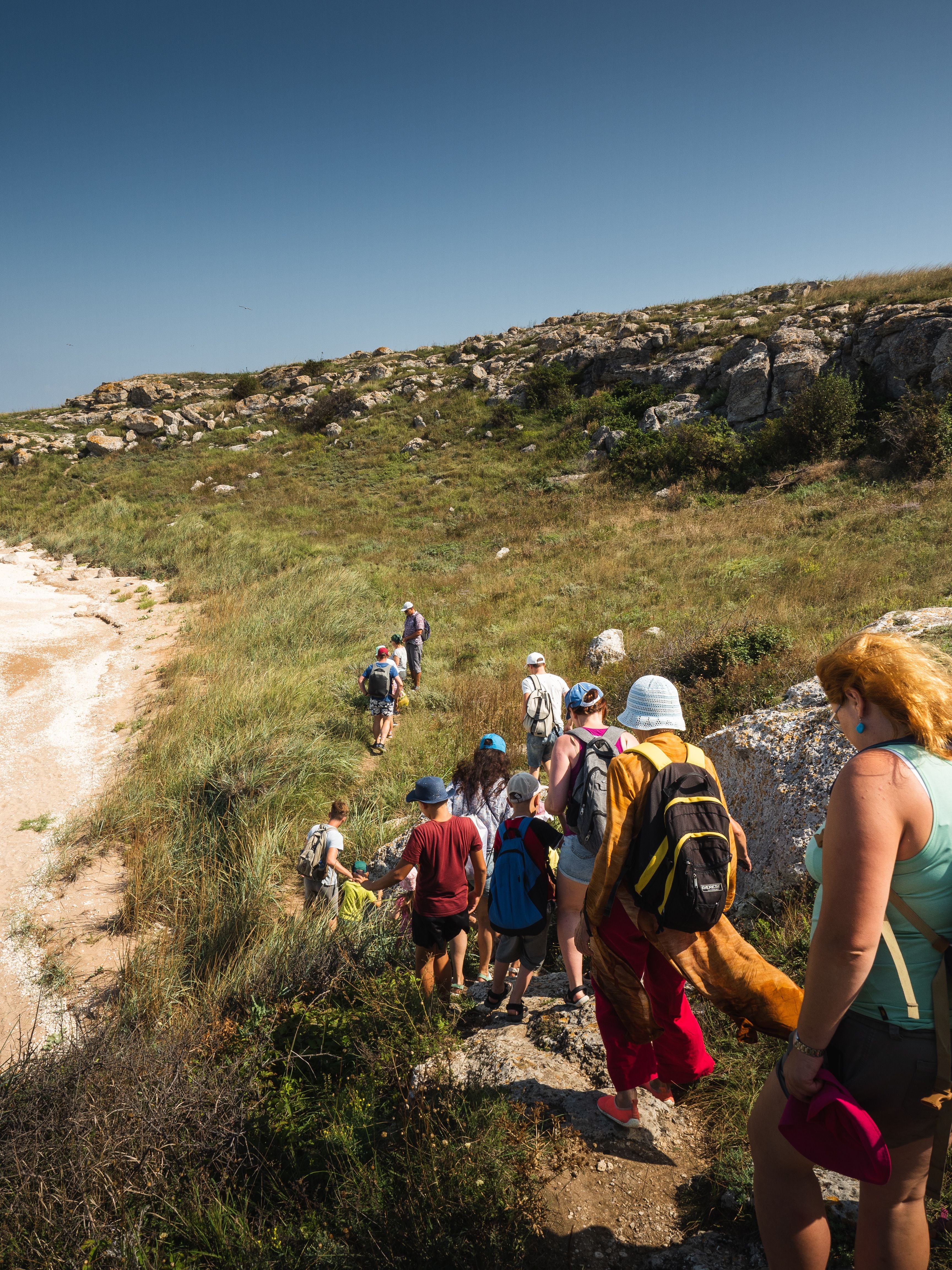 Group of hikers seen from behind following a narrow trail across a rocky hillside.