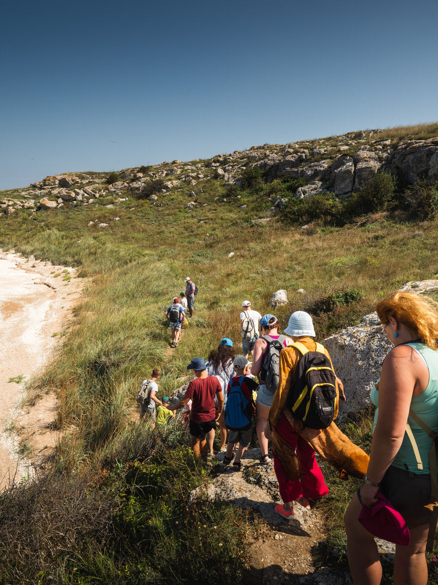 Group of hikers seen from behind following a narrow trail across a rocky hillside.