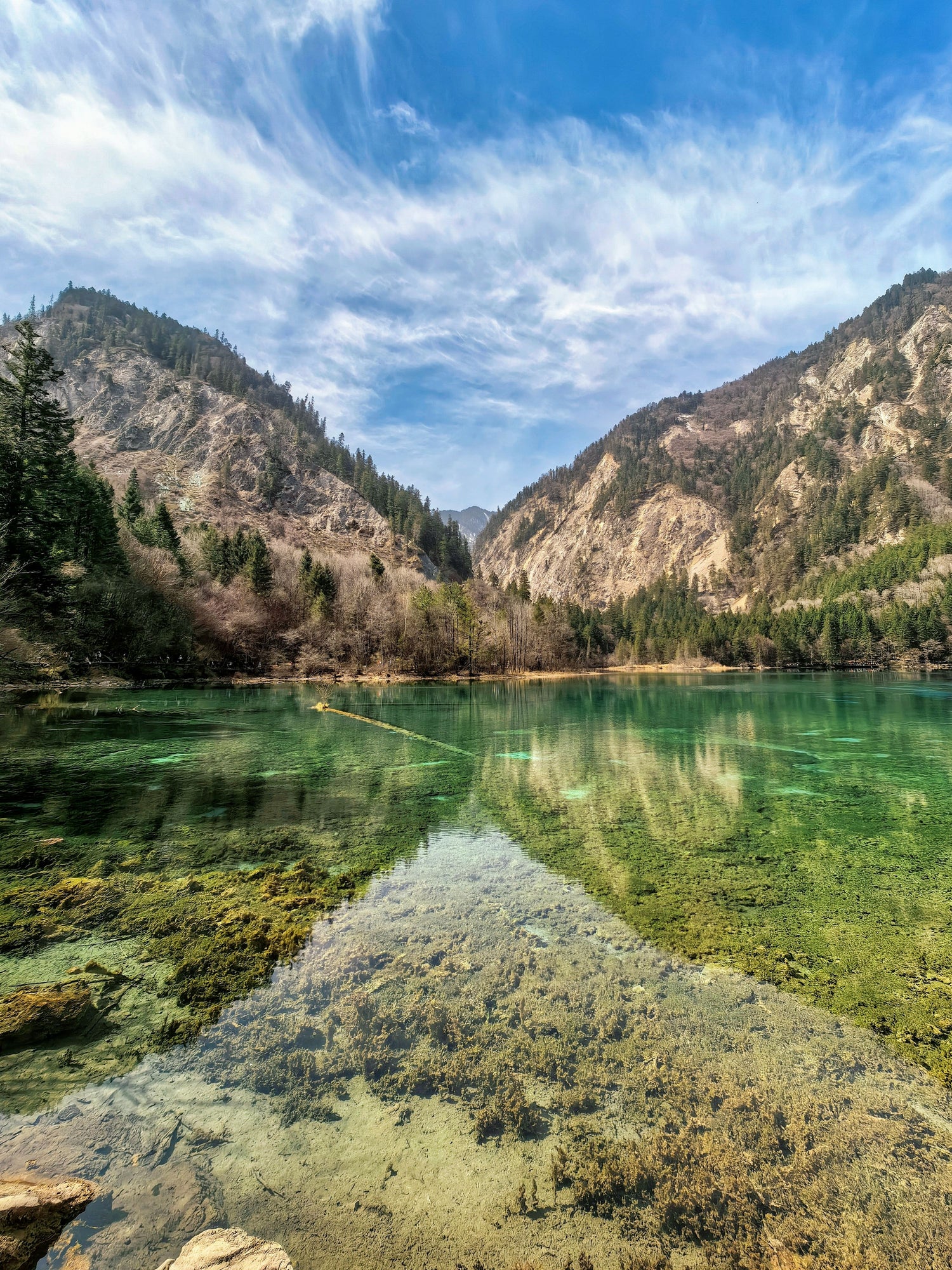 Calm lake below forested mountains and a broad sky in Jiuzhaigou Valley.