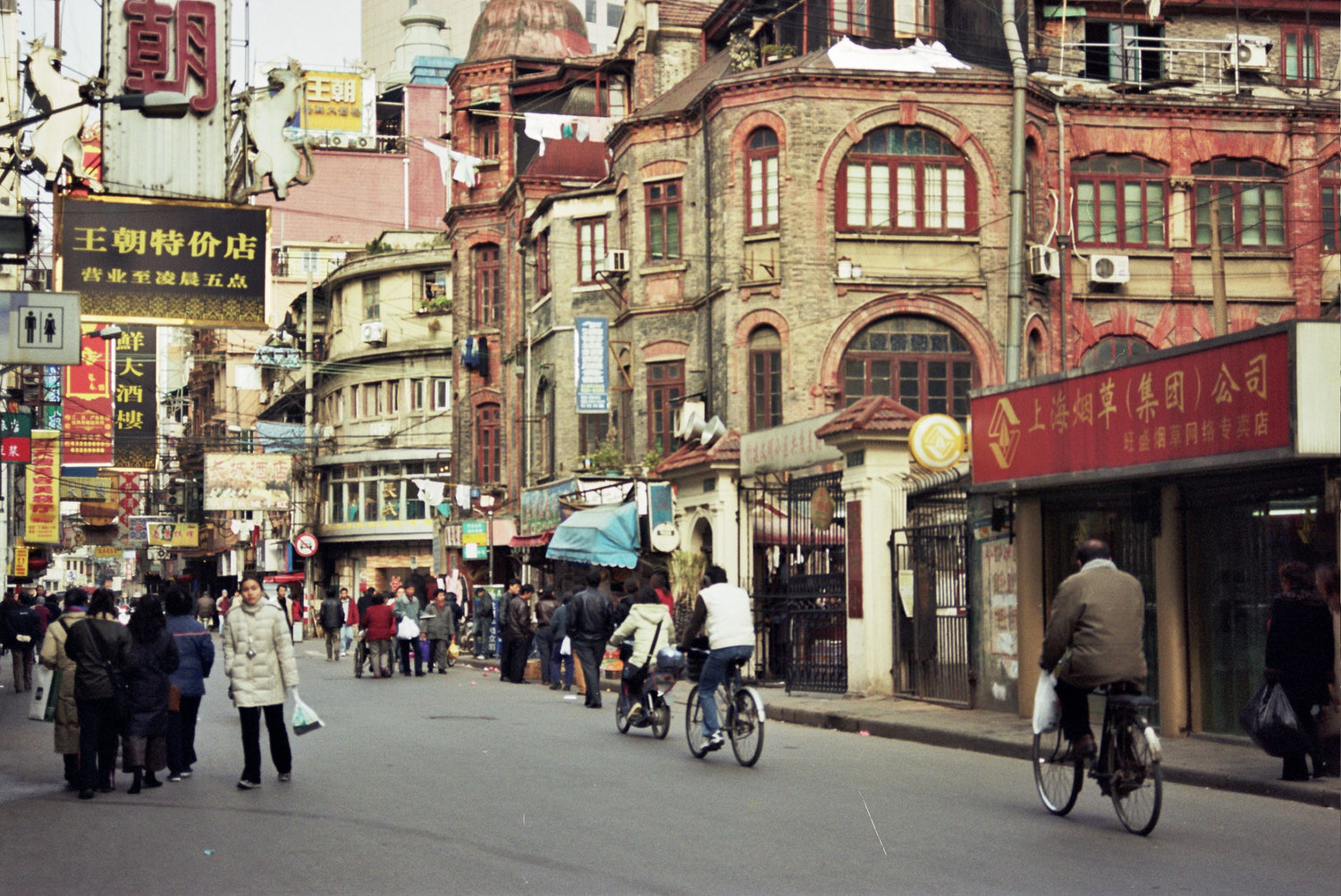 Pedestrians and cyclists moving along a historic Shanghai street lined with shophouses.