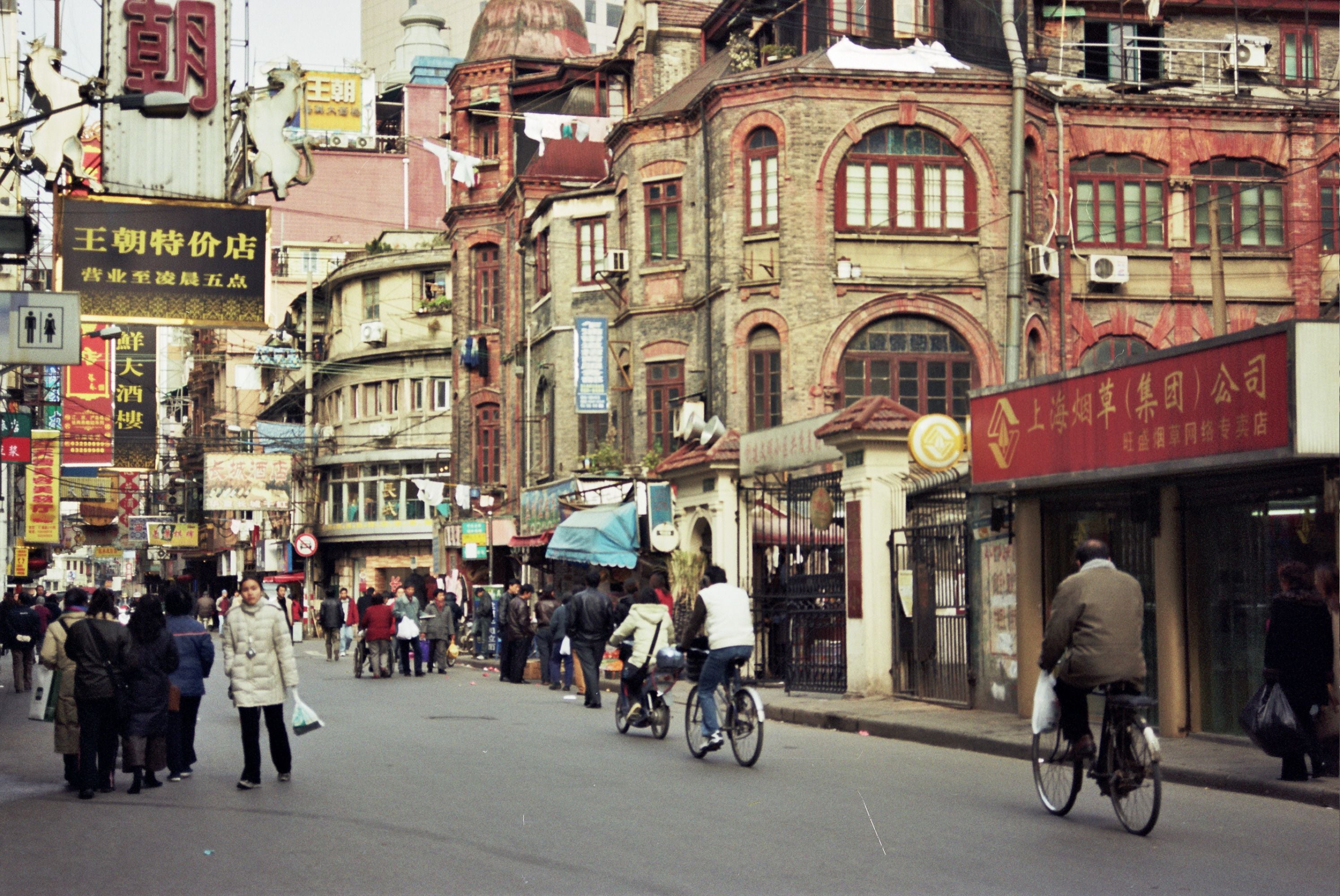 Pedestrians and cyclists moving along a historic Shanghai street lined with shophouses.