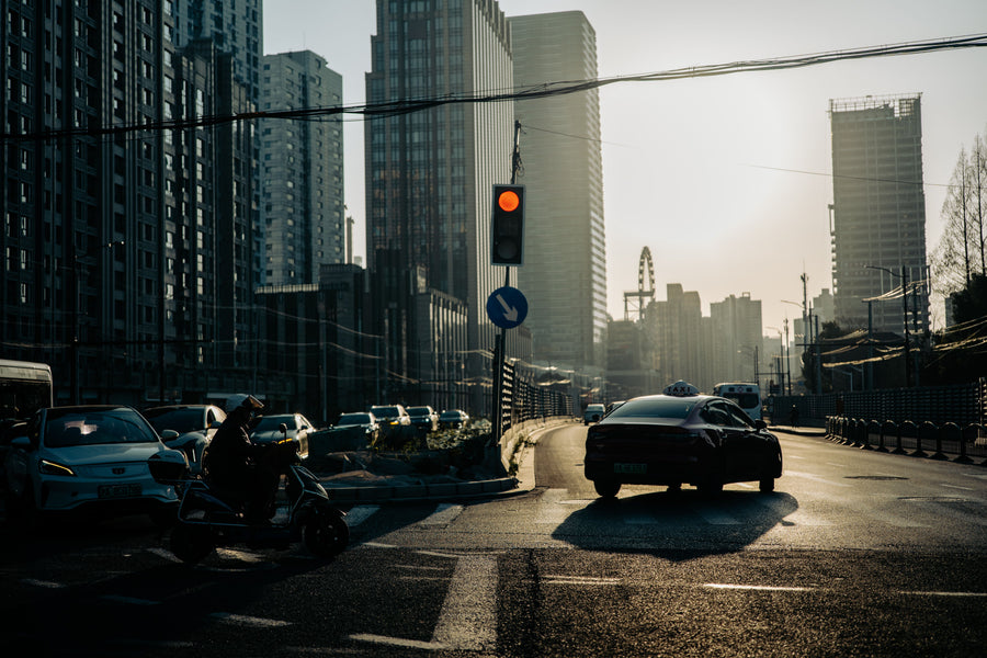 A helmeted scooter rider and cars crossing a Shanghai street in warm dusk light.