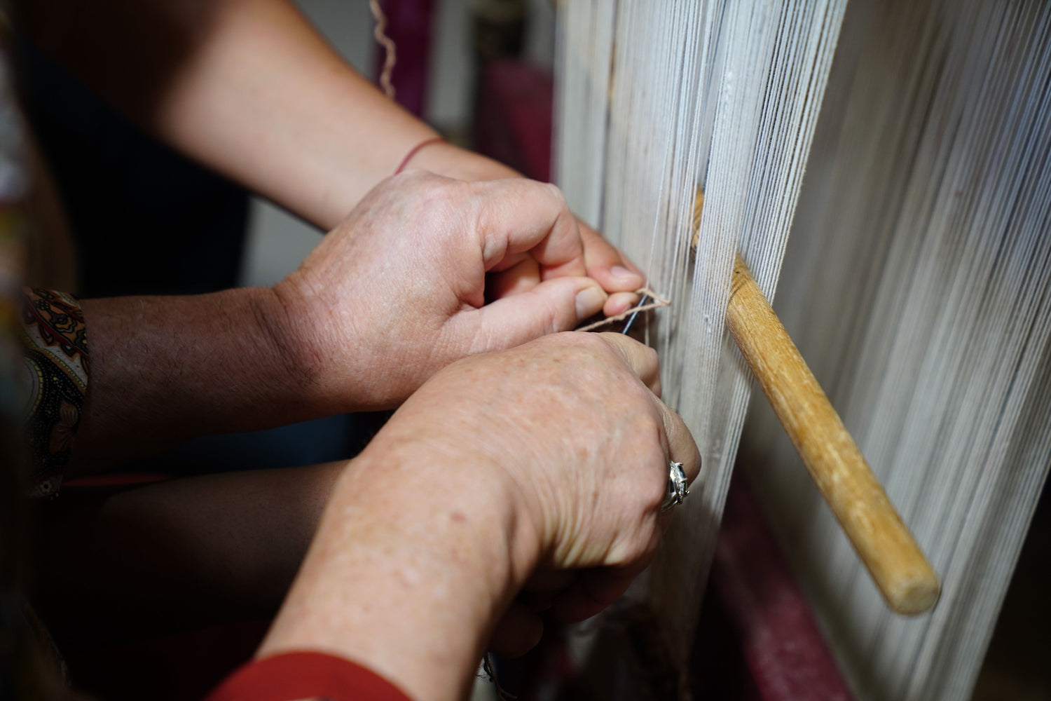 Hands guiding threads on a traditional loom.