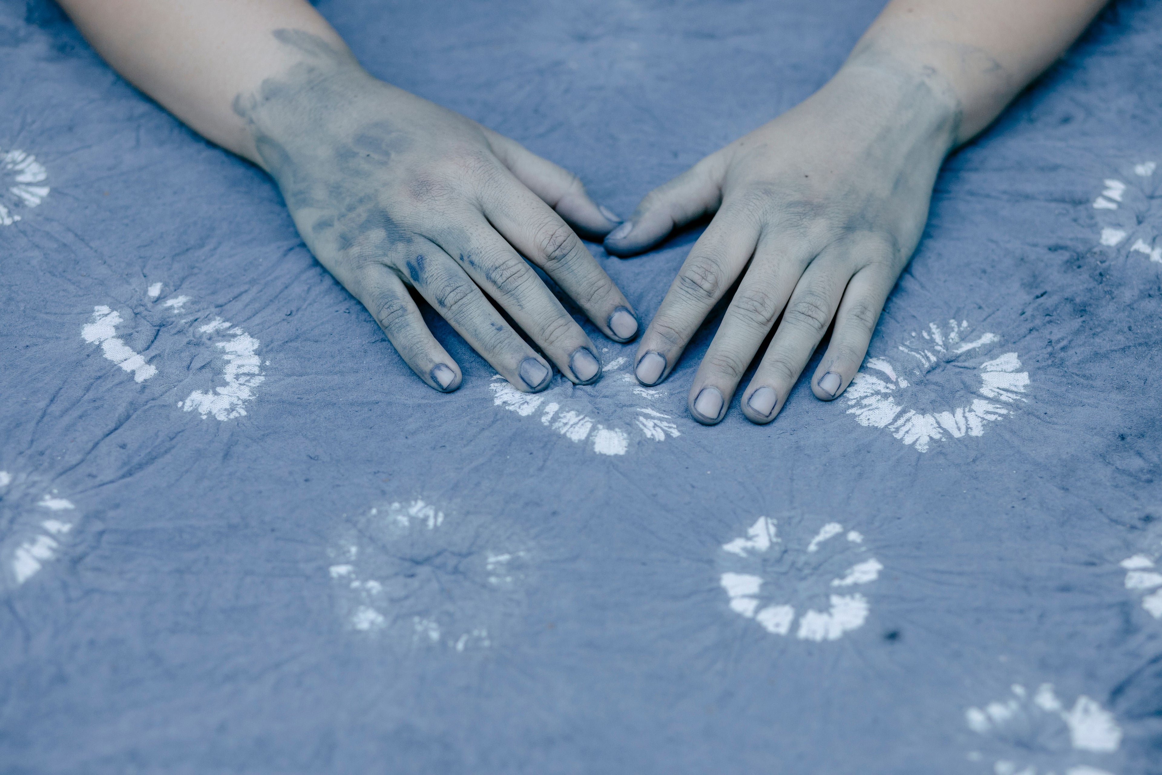 Indigo-stained hands resting on pale-blue resist-dyed patterned fabric.
