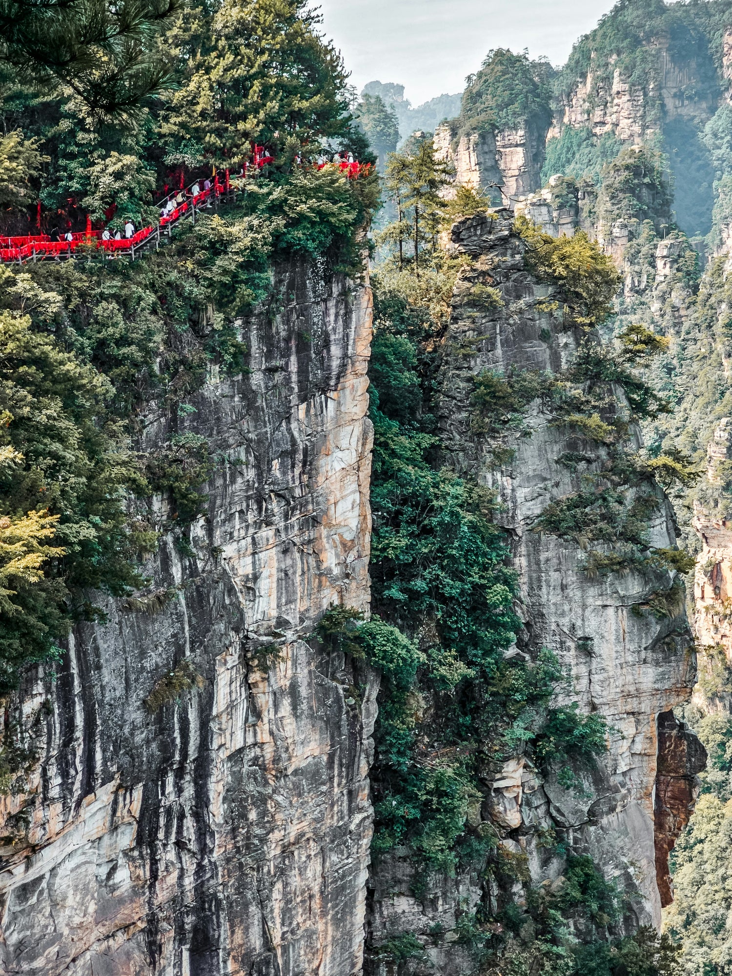 Visitors walking a cliffside path among sandstone pillars in Zhangjiajie National Forest Park.