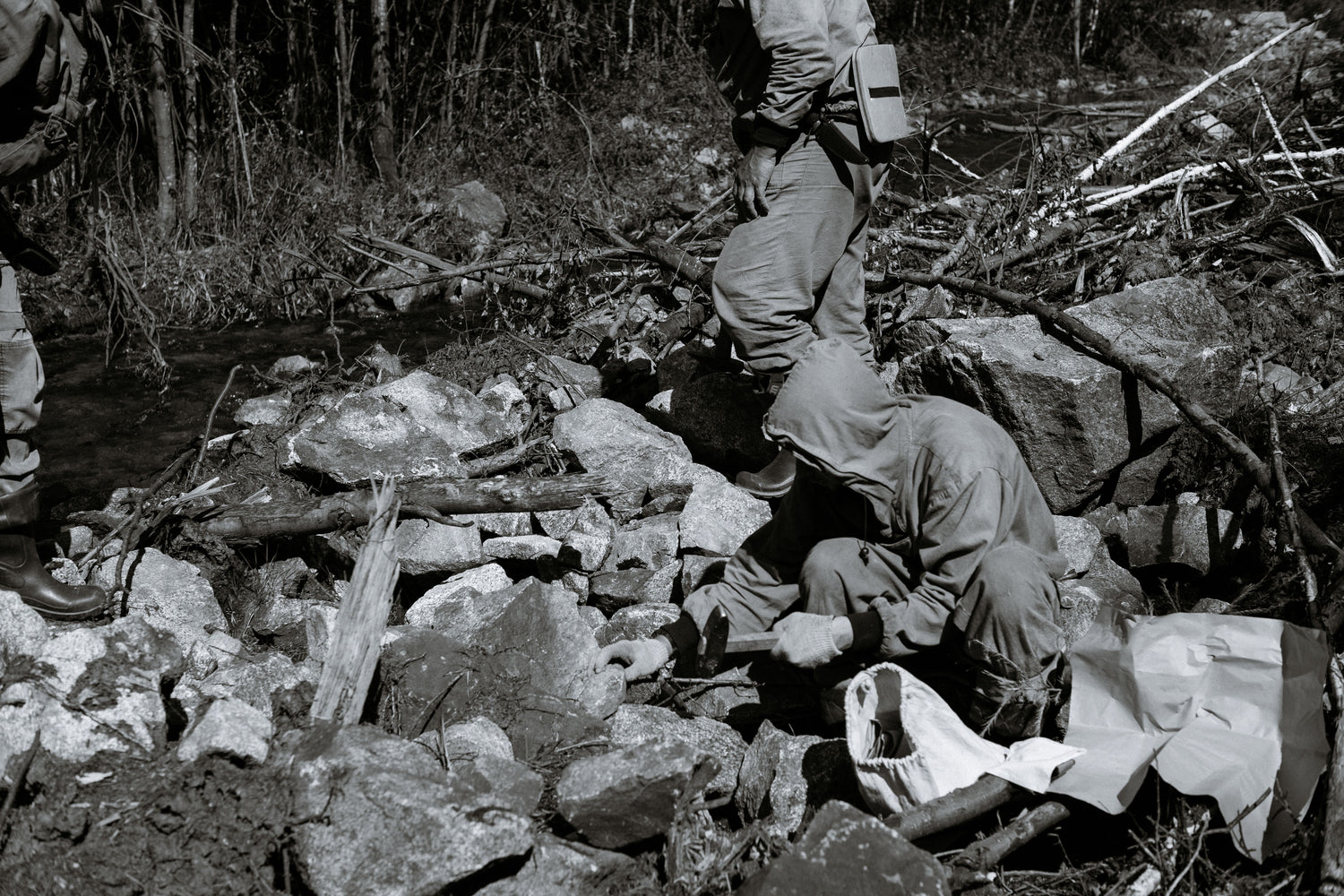 Geologists crouching among rocks and using field tools during an outdoor terrain study.